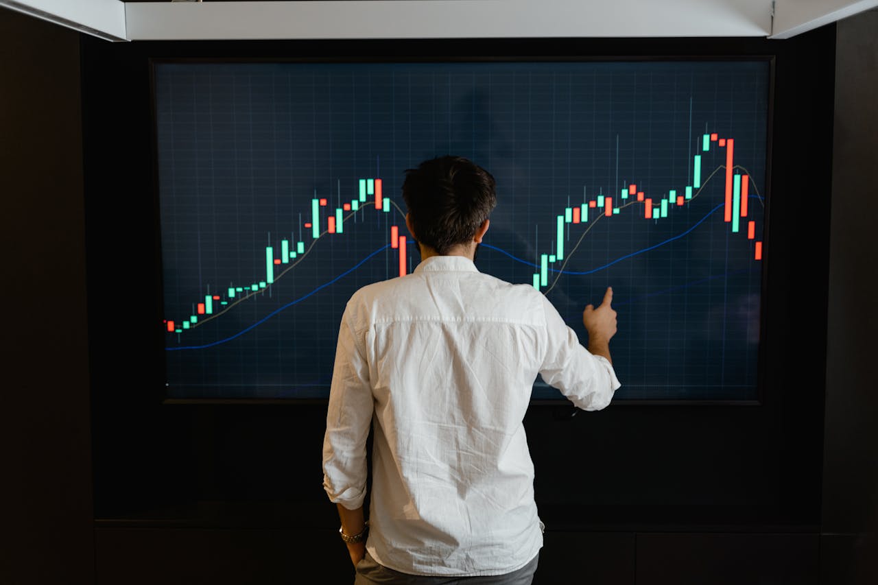 Services Adult male reviewing stock market data on a large display screen indoors.